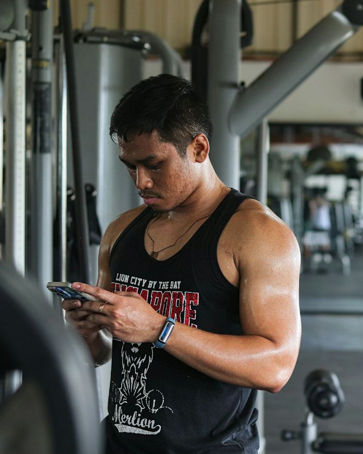 Homem forte de regata olhando o celular na academia