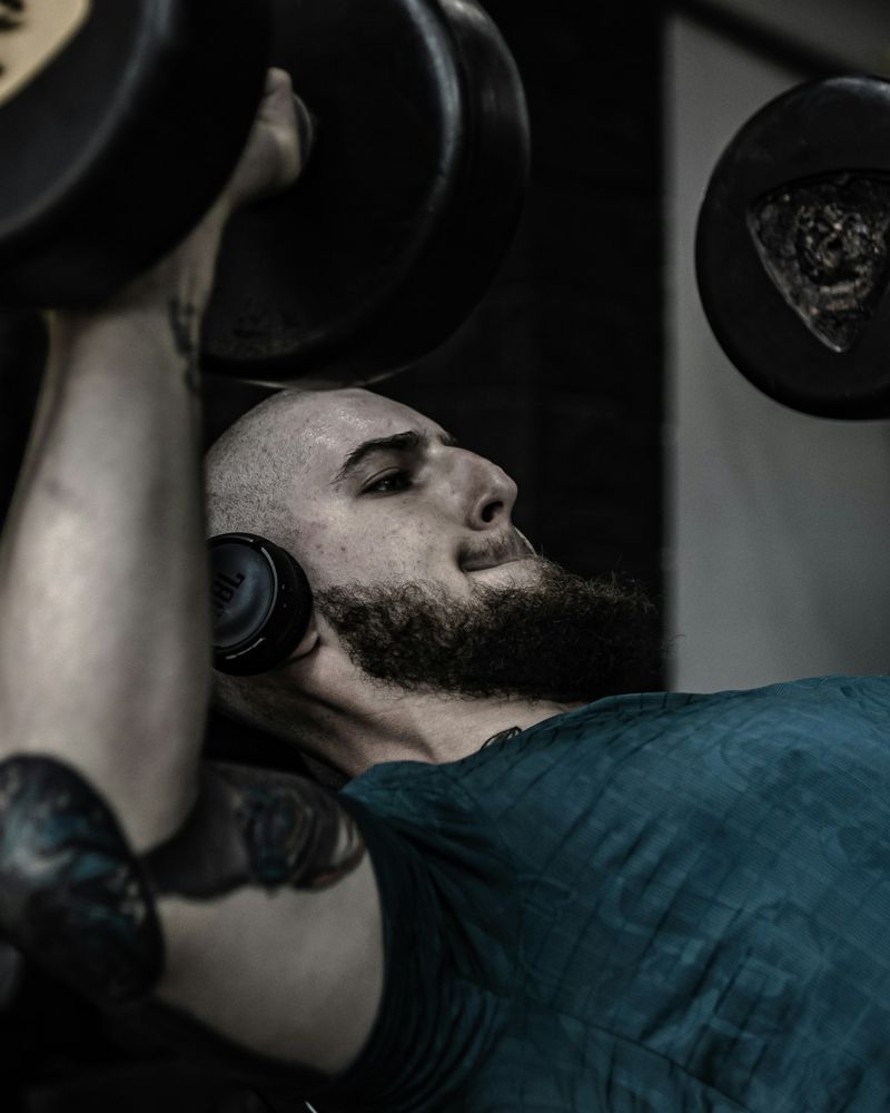 Homem de barba fazendo supino com halteres, em close